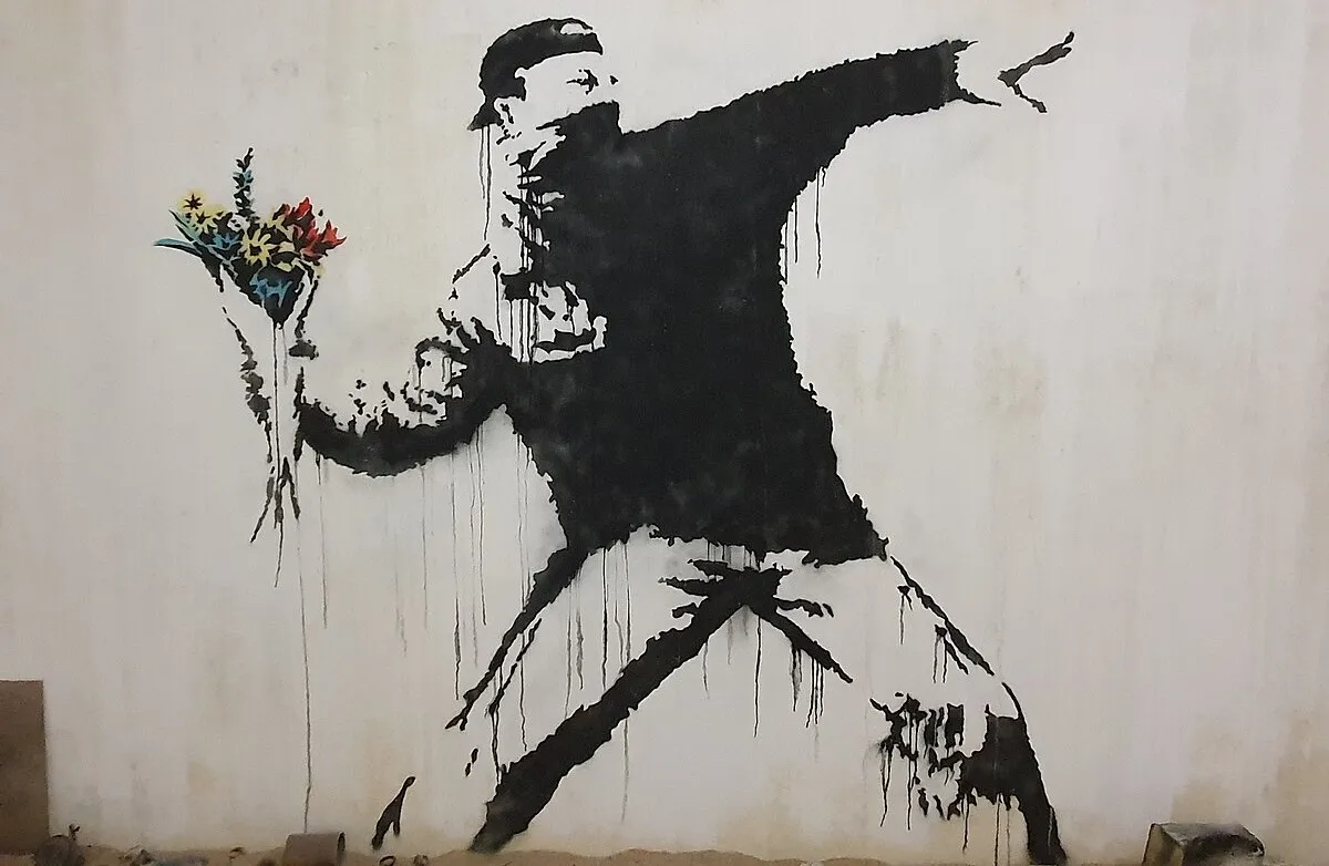 This is an image of the famous artwork "Flower Thrower" by the artist Banksy. The piece depicts a person in a protest-like stance, preparing to throw a bouquet of flowers. It's a well-known example of Banksy's street art, which often contains political and social messages.