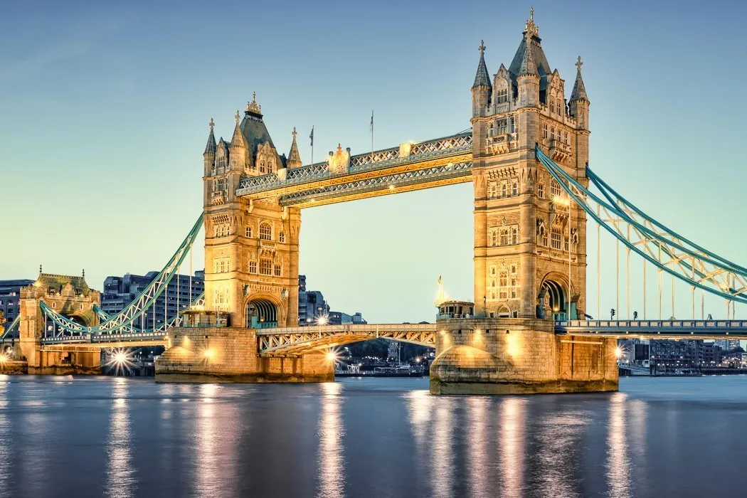 A view of Tower Bridge in London
This image shows the famous Tower Bridge and the river Thames, which are iconic symbols of London.

--- Image Analysis ---
This image is a simple photograph with no embedded data, statistics, or text.

1.  **Data & Statistics**: None visible.
2.  **Text Content**: None visible.
3.  **Visual Structure**: The image is a photograph depicting the Tower Bridge in London, United Kingdom, at what appears to be dusk or dawn. The bridge is prominently featured, illuminated by artificial lights, which reflect on the calm water of the River Thames below. The iconic Gothic-style towers and the suspension elements are clearly visible, with a lighter sky in the background and some city buildings faintly visible on the banks.
4.  **Key Takeaways**:
    *   The image shows the famous Tower Bridge, a landmark in London, England.
    *   The bridge is illuminated, suggesting it's a nighttime or twilight scene, and its lights reflect beautifully on the water.
    *   It highlights the architectural grandeur and iconic status of the Tower Bridge.