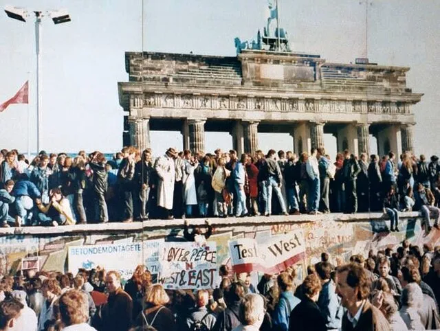 Menschenmengen auf der Berliner Mauer Ende 1989 nach dem historischen Mauerfall. Im Hintergrund das Brandenburger Tor, Symbol der Wiedervereinigung Deutschlands